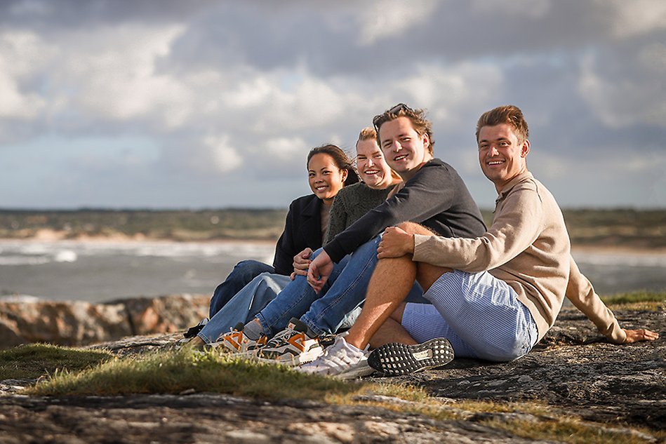 A group of young people sitting on the cliffs by the beach. Photo.