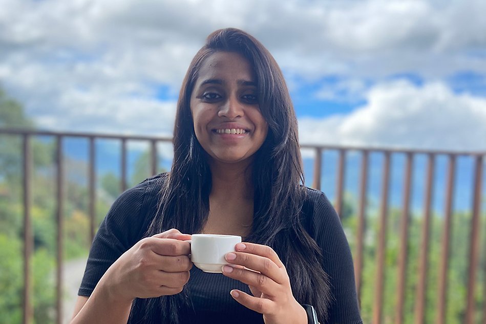 Young woman holding a coffee cup with an ocean view in the background. Photo.