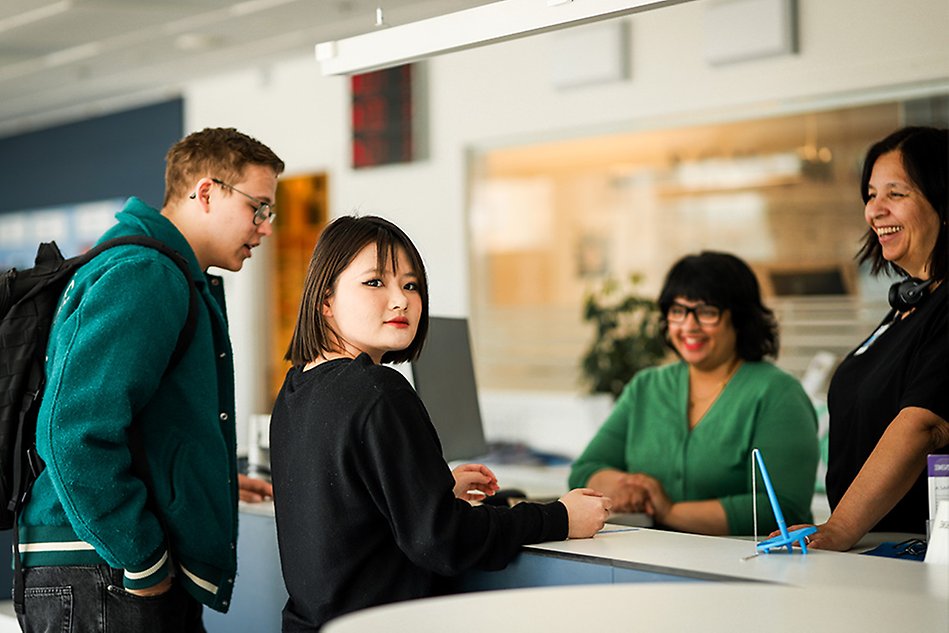 Two students are talking to two persons behind a reception desk. photo.